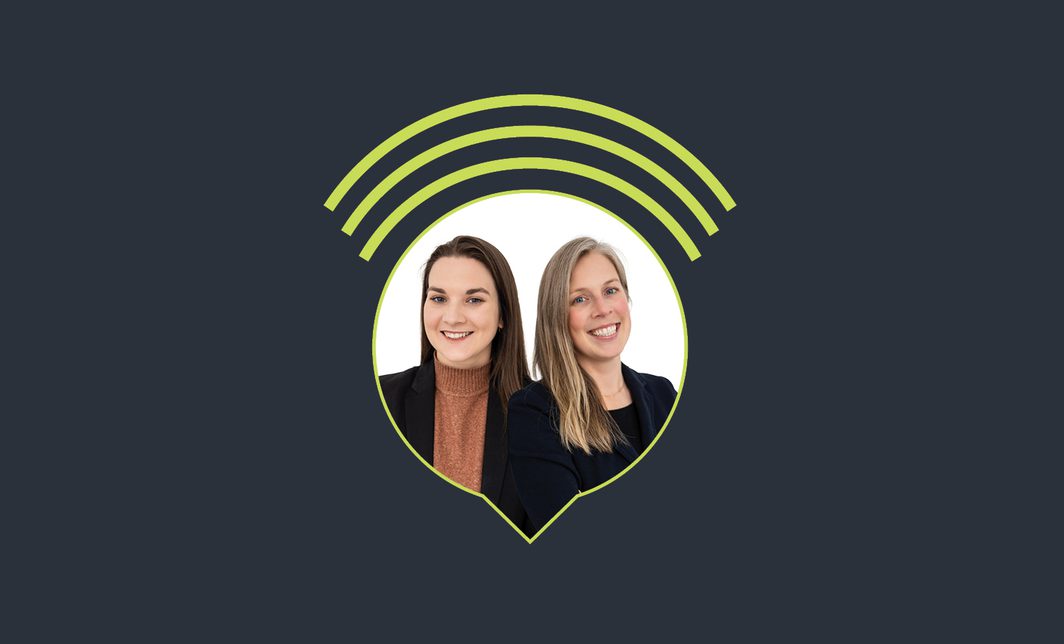 Two female podcast hosts in suits, smiling.