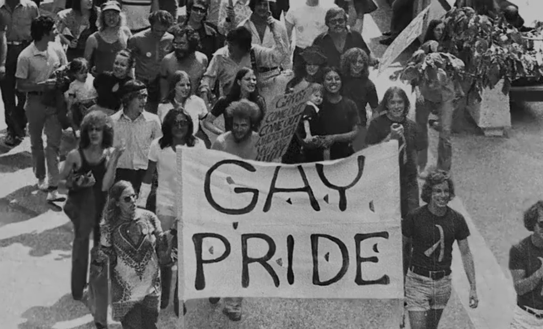 A black and white photo of a crowd holding a sign that says 'gay pride.'